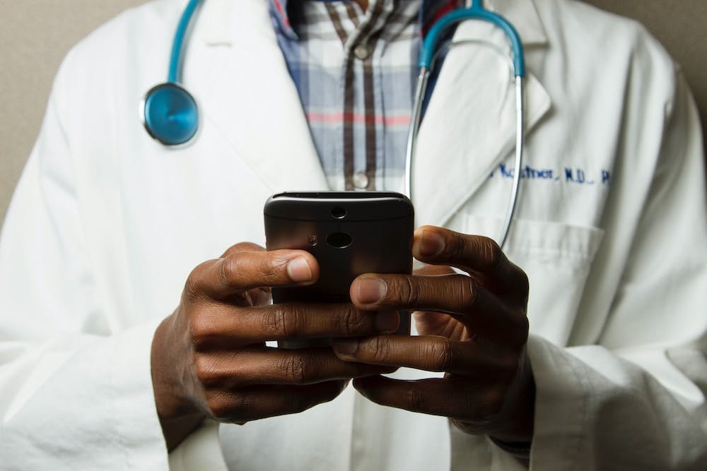 Doctor in medical jacket with stethoscope holding a phone. 
 
Photo by National Cancer Institute on Unsp