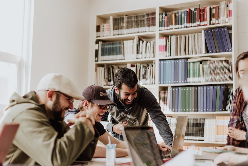 three men laughing and looking at a computer in an office. Photo by Priscilla Du Preez on Unsplash