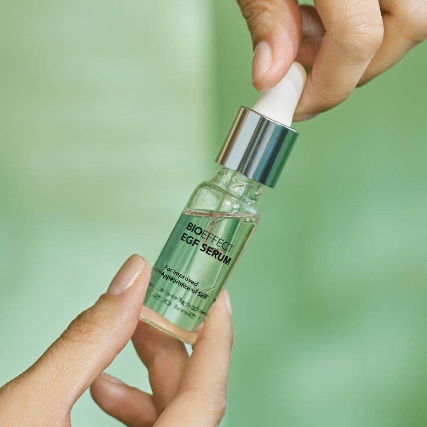 A person holding a bottle of BIOEFFECT EGF serum in front of a green background.