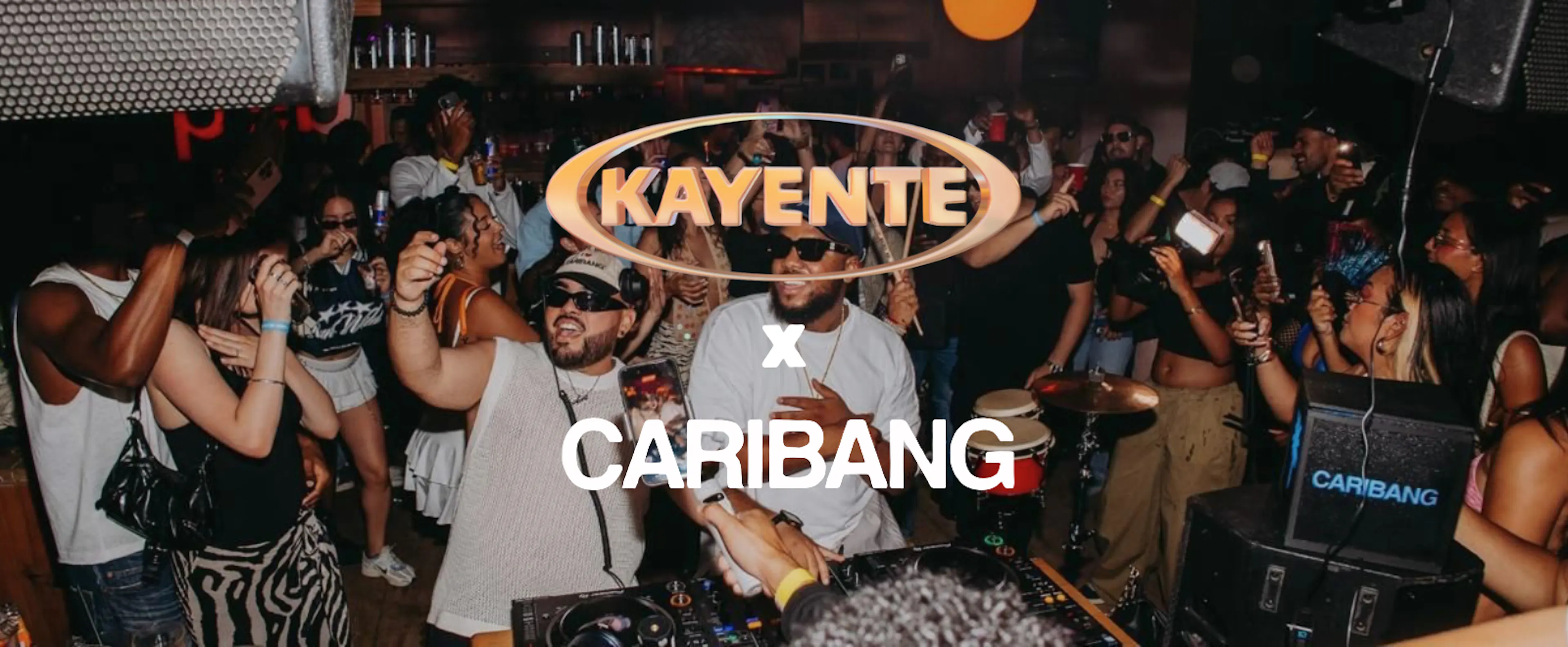 Mensen dansen in de club, met de logo's van Kayente en Caribang