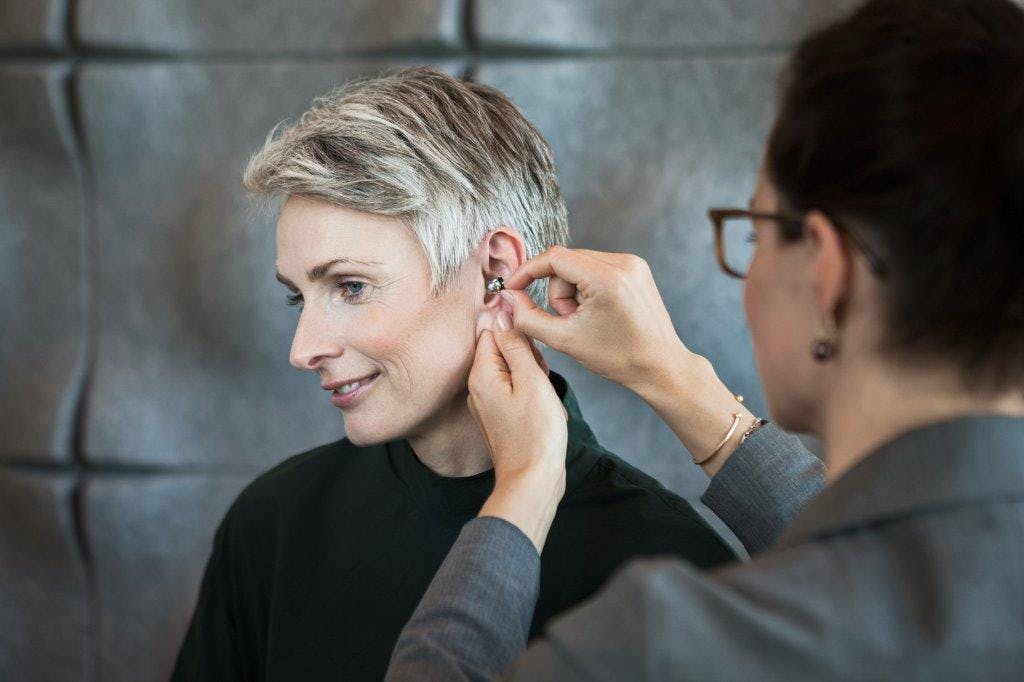 Woman helping other woman try on a hearing aid