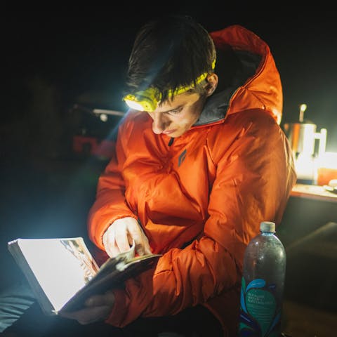 Black Diamond athlete Connor Herson reads the "Creek Freak", Indian Creek climbing guidebook at camp using a black diamond headlamp.