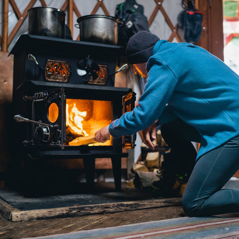 A backcountry Skier stokes a fire to keep the yurt warm. 