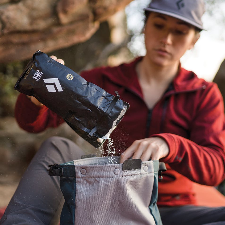 Climber at a boulder pouring Black Diamond Black Gold Chalk into a chalk bag