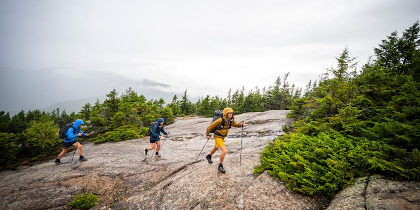 Three hikers in Beta Light Packs and wearing Stormline Shells trek across a granite dome. 