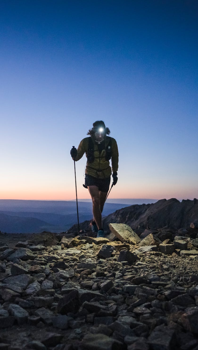 Black Diamond athlete Joe Grant running in a dark scree field with a Black Diamond headlamp and trekking poles.