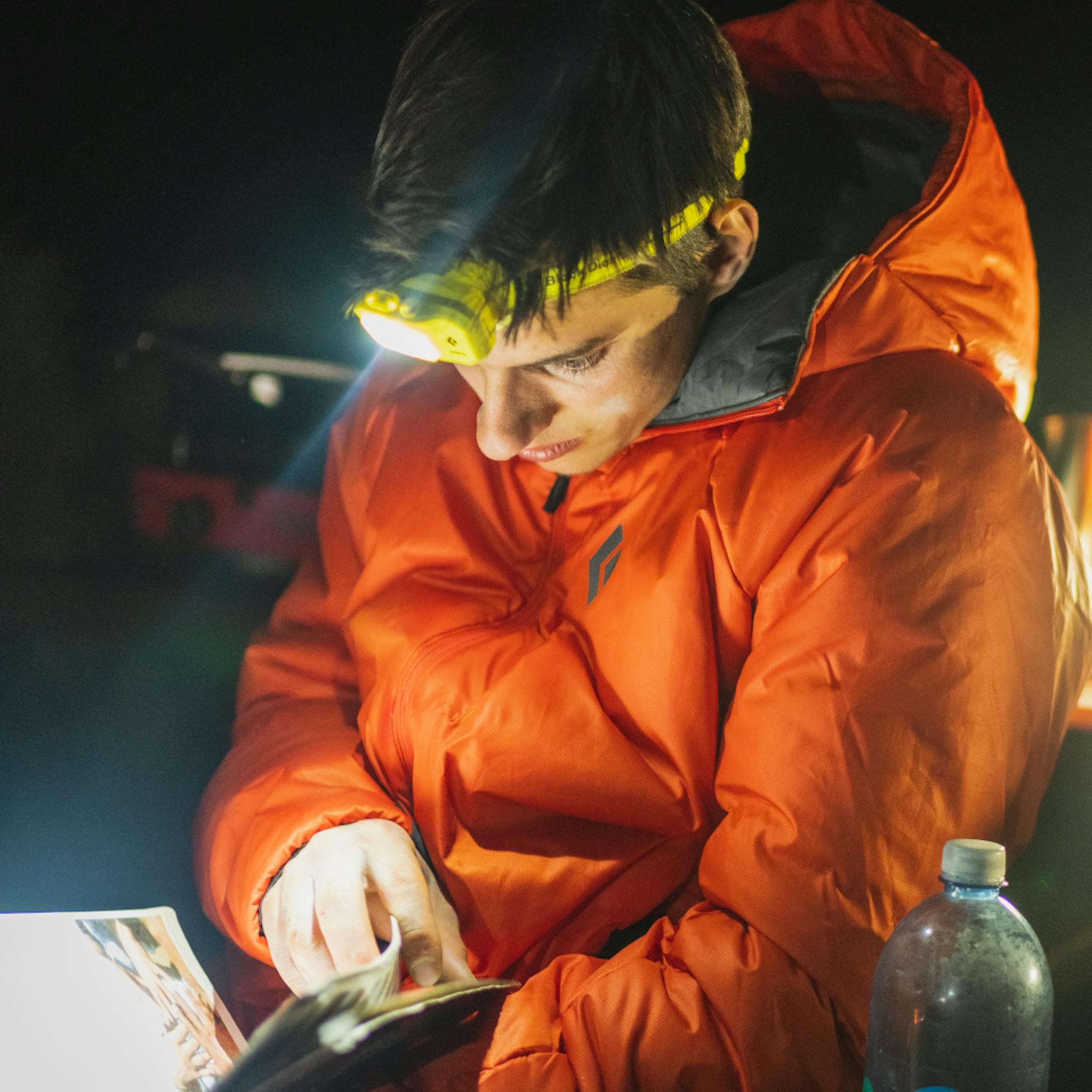 A climber bundled up in a Belay Parka looks at a guidebook at night.