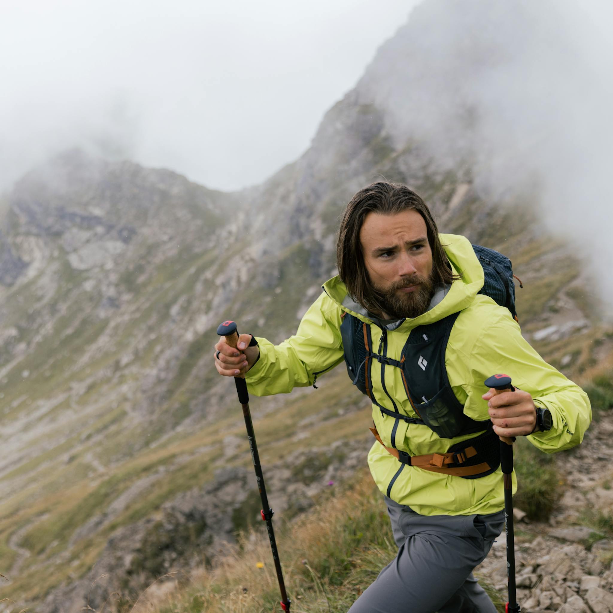 A hiker with BD trekking poles hikes up a steep, foggy hill.
