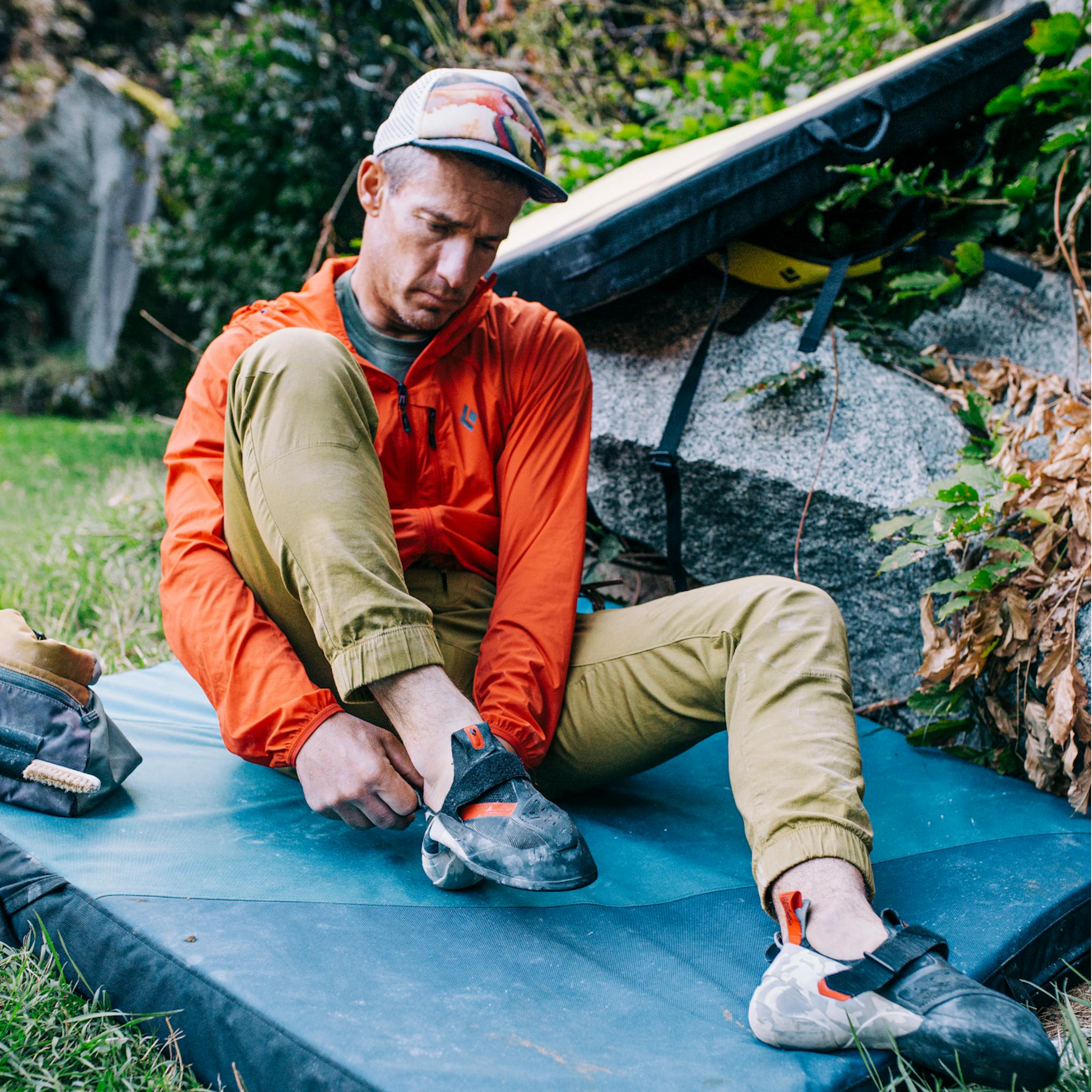 A climber slips on their rock shoes wearing the Black Diamond Notion Pants.