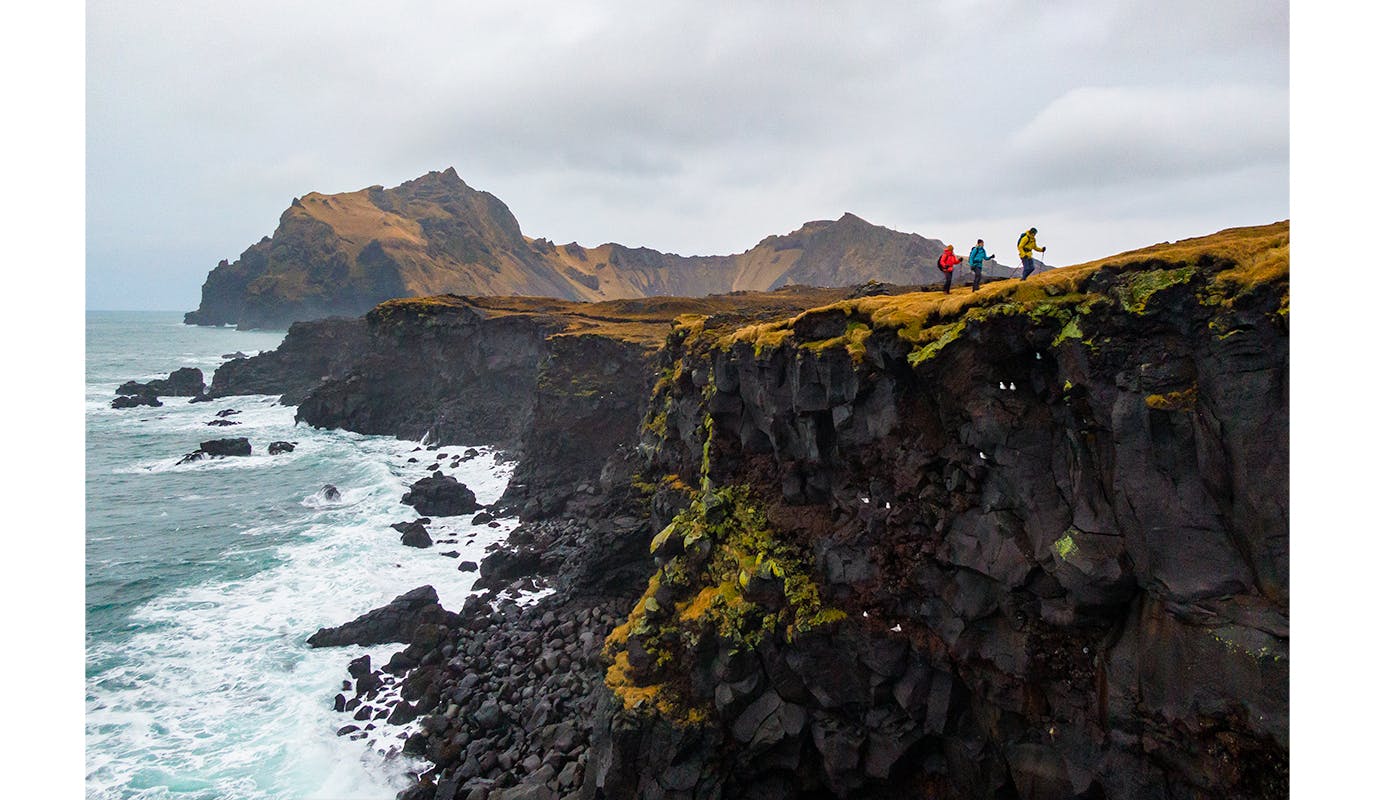Three Hikers walk above a costal cliff in Iceland wearing Black Dimaond Technical rain shells to stay dry on a cold drizzly day.