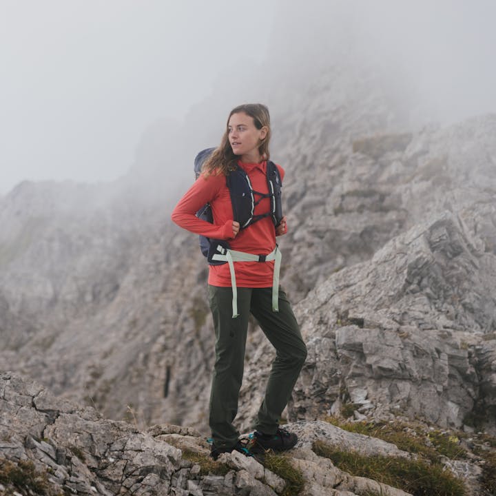 A hiker stands on a ridgeline wearing the Black Diamond Pursuit Pack and an Alpenglow pro sun hoody.  