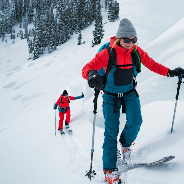A skier grinning ear to ear and in a Black Diamond Recon Stretch Bibs tours up a steep incline. 