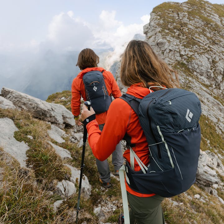 Two hikers wearing Black Diamond Pursuit Packs walking along a rocky mountain trail. 