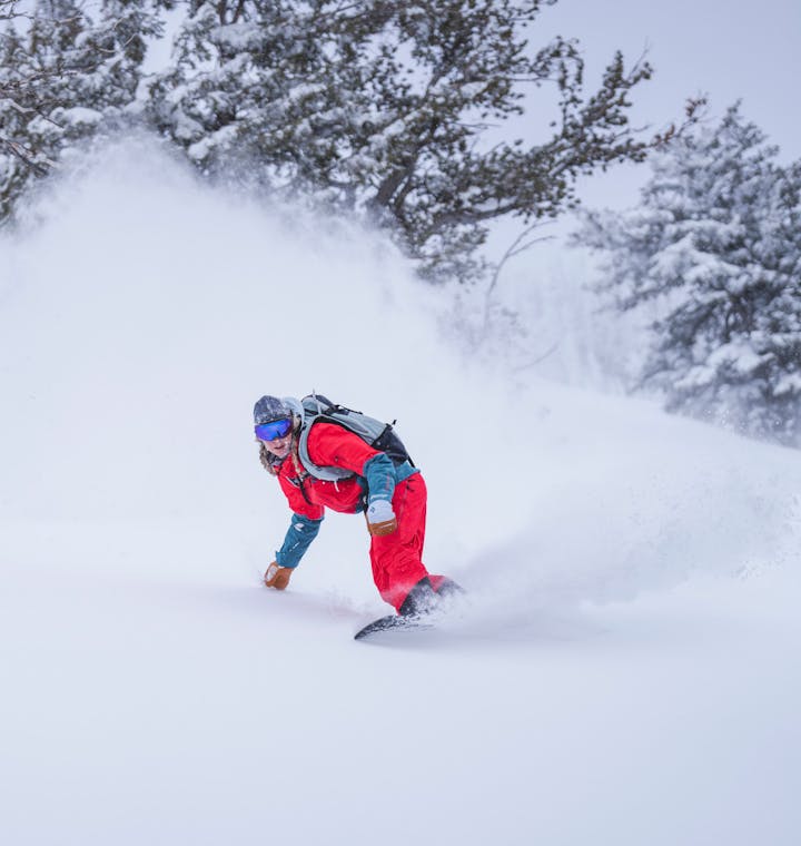 Women's Ski Apparel. A snowboarder makes a powder turn.