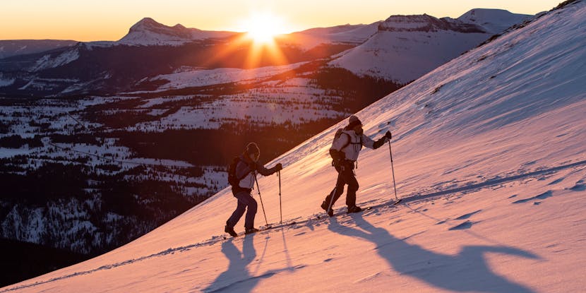 Zwei Freerider bei einer Skitour mit Sonnenaufgang im Hintergrund. 