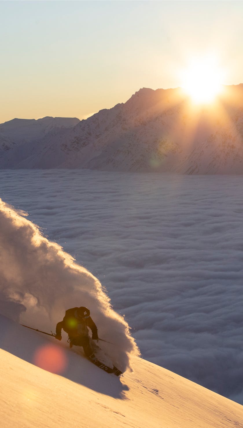 Ein Skifahrer bei der Abfahrt, während im Hintergrund die Sonne aufgeht. 