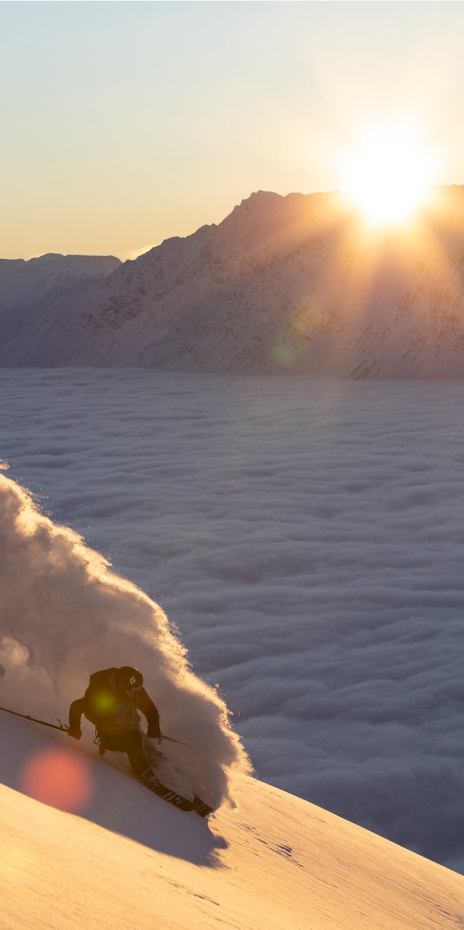 Un skieur effectue sa descente tandis que le soleil se lève au loin.
