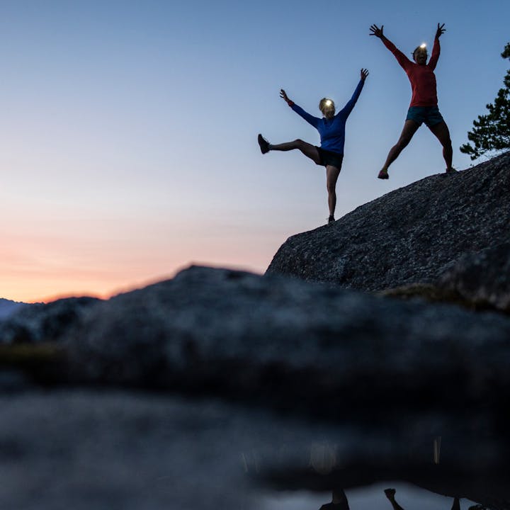 Two climbers jump for joy at twilight in BD headlamps.