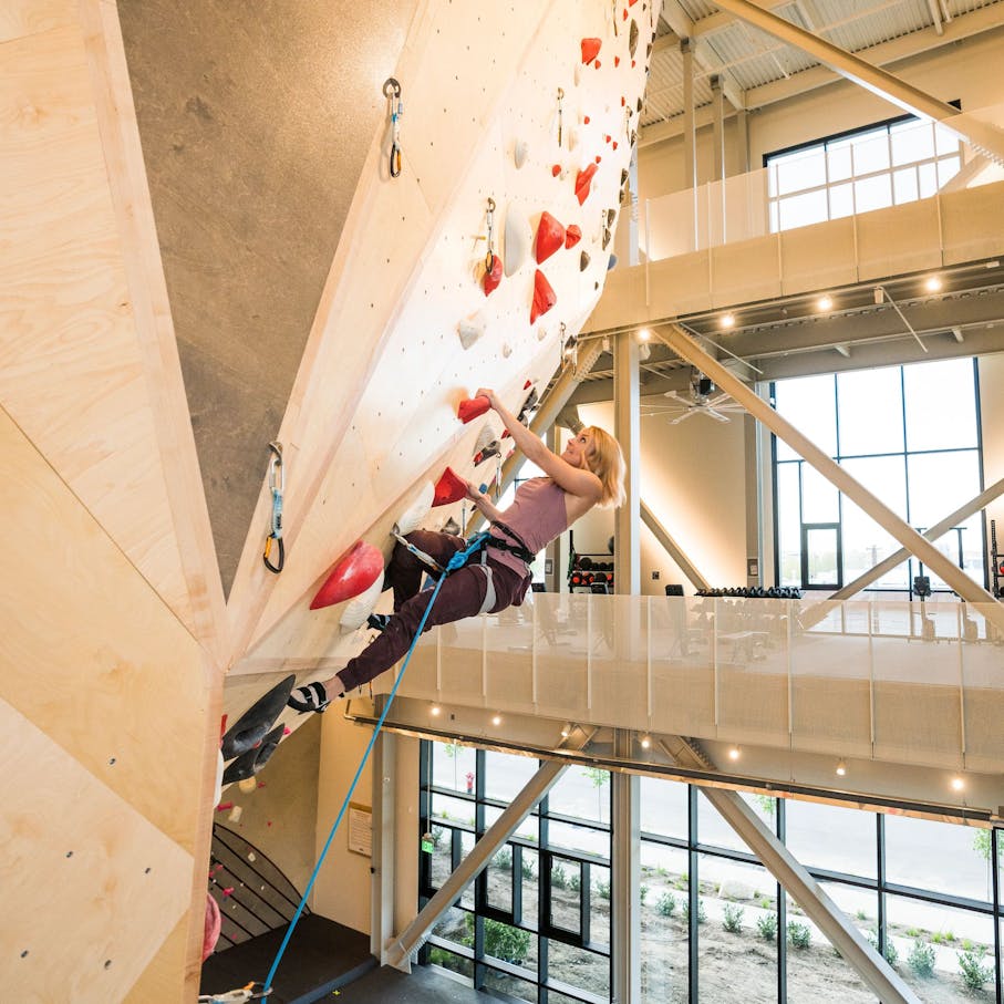 Woman climbing in BD gear and the Women's Momentum climbing shoe in a climbing gym on an overhanging section