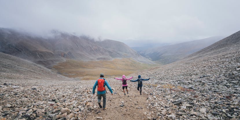 Three hikers run down a scree mountain in their Black Diamond Approach shoes and insulation. 