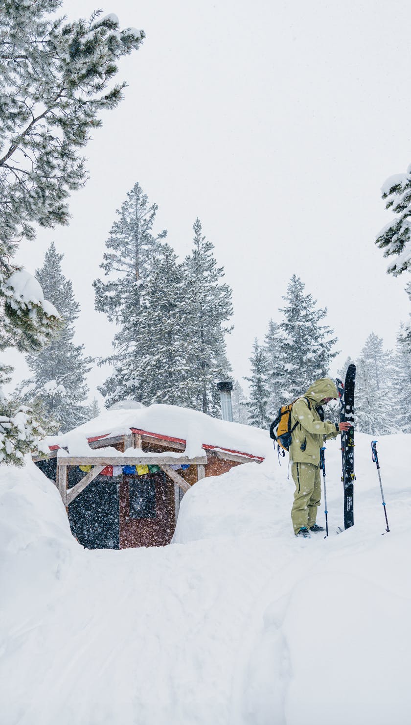 Gifts that go beyond. A skier stands in front of a snow covered backcountry yurt during a snow storm. 