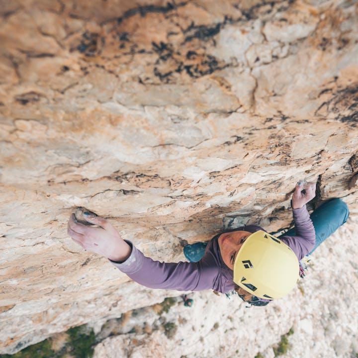 A climber in a yellow Black Diamond Capitan Helmet crimps a hold as she works her way up a climb. 