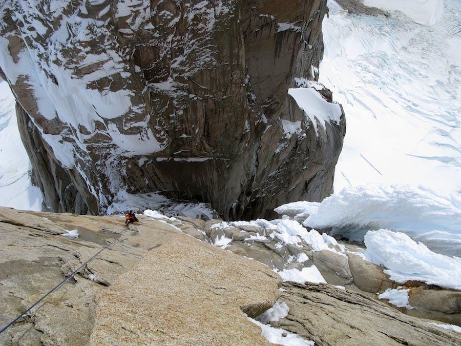 Climbing a large sheer rock face, surrounded by snow