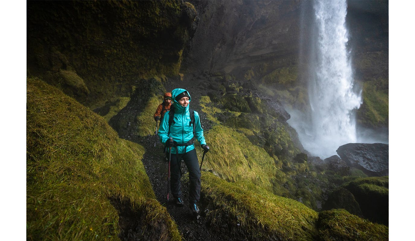 a couple of hikers walking past a waterfall wearing Black Diamond technical rain shells to stay dry. 