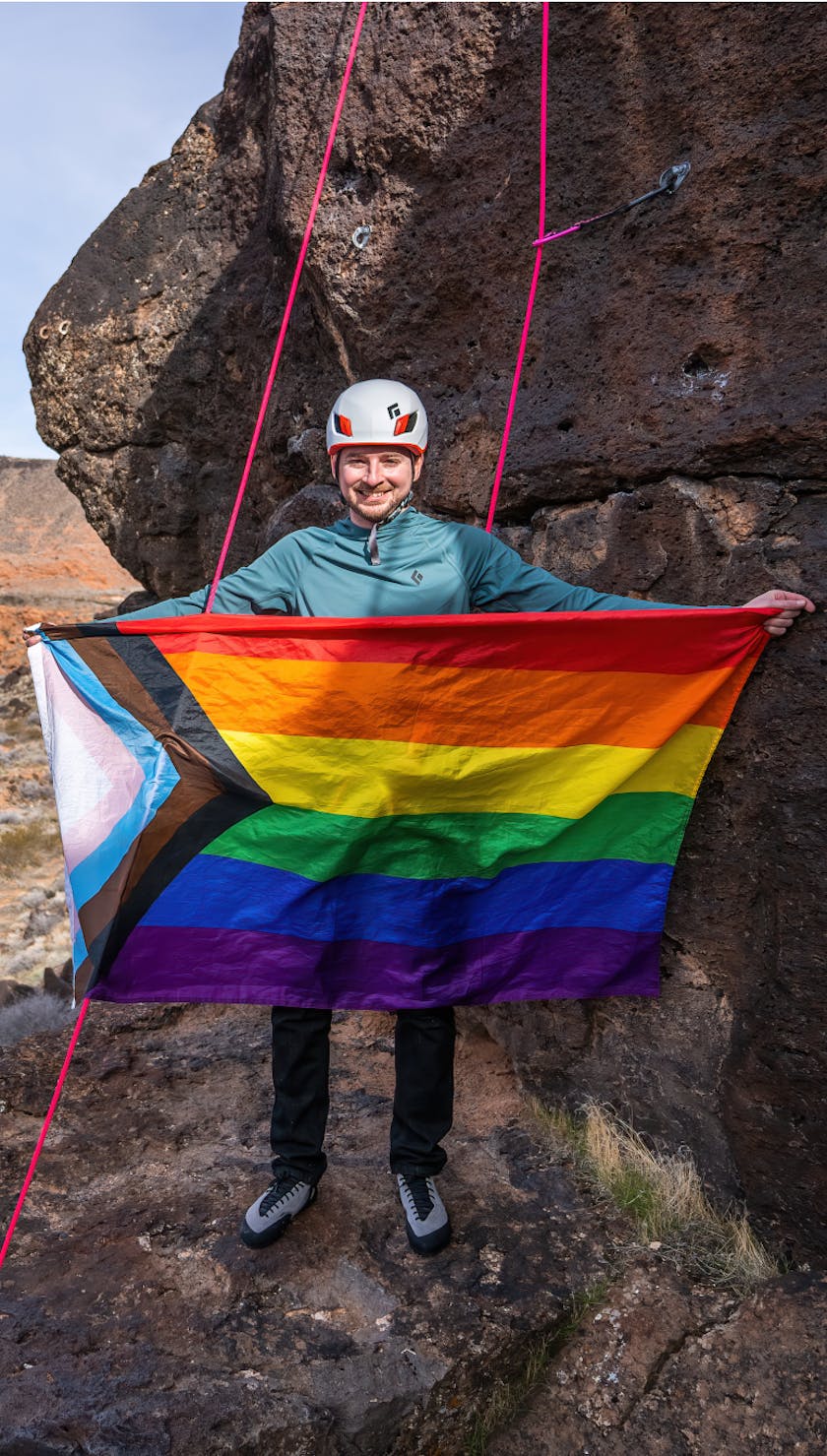 Black Diamond Ambassador holding a Pride flag at the crag.