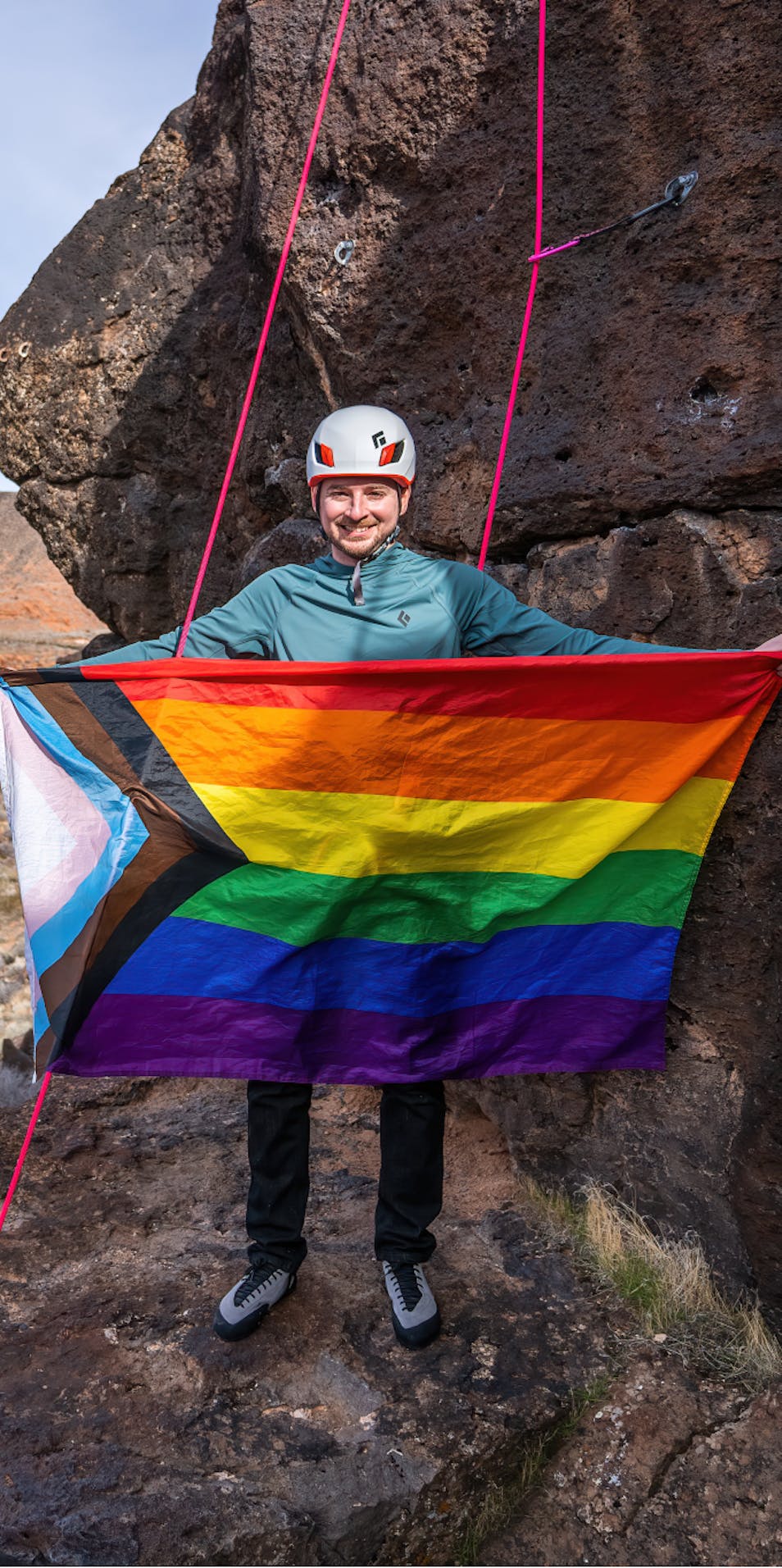 Black Diamond Ambassador holding a Pride flag at the crag.