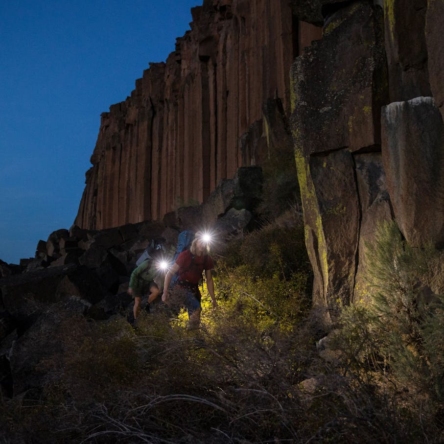 Two climbers in front of climbing wall on the approach wearing BD headlamps at dawn