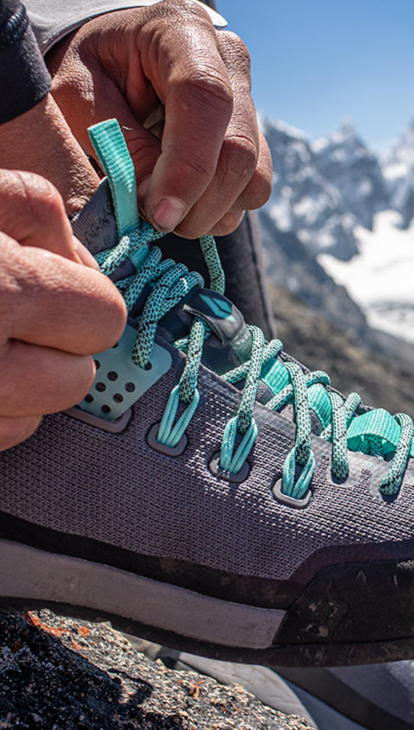 woman tying her approach shoes on a trail in the mountains.