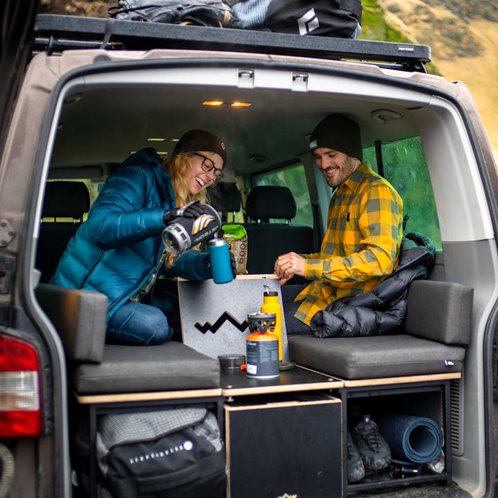 A couple of friends enjoy making coffee in a camper van wearing Black Diamond Apparel. 