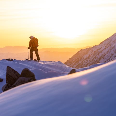 A backcountry skier rounds the top of the mountain in the rising dawn sunlight.