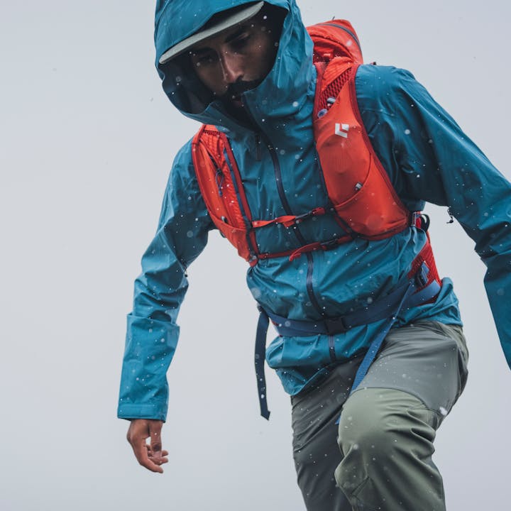 A hiker treks through rain in a Black Diamond Stormline Stretch Rain Shell. 