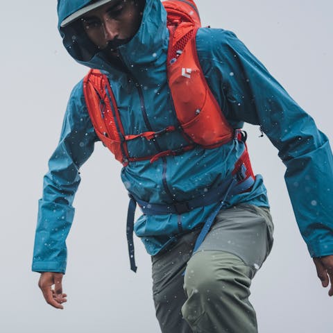 A hiker steps up on a rock in the rain, but his Black Diamond Stormline Shell is keeping him dry. 