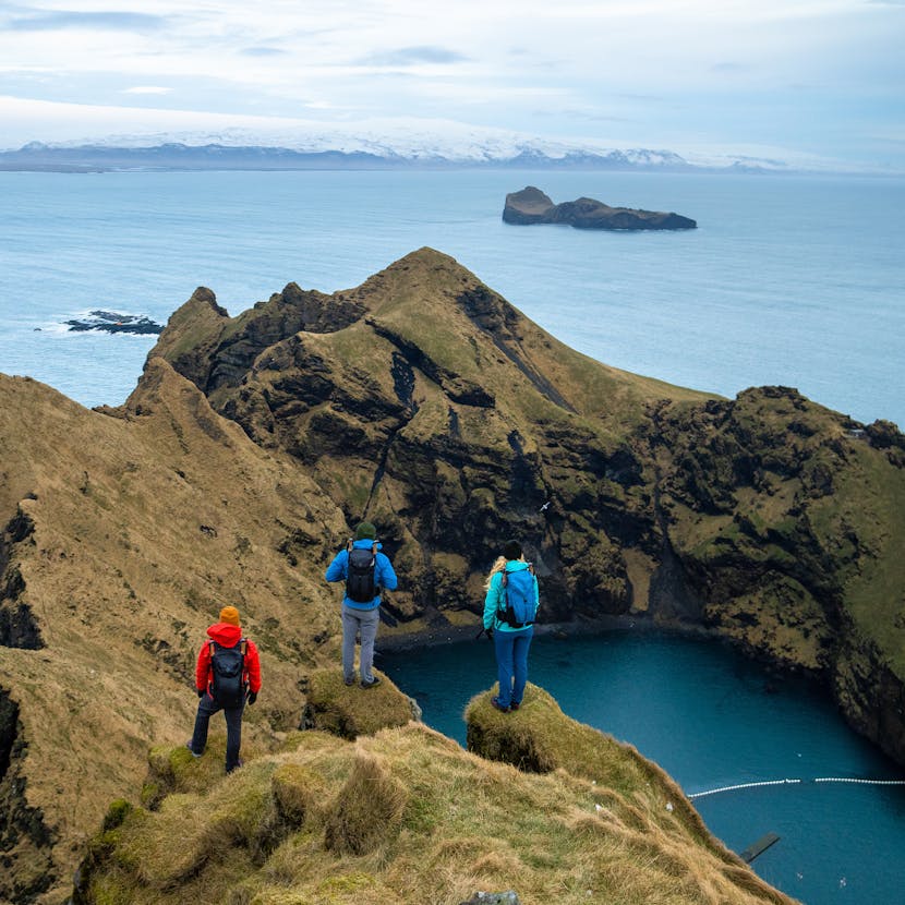 Three hikers take in an ocean view from atop a mountain in Iceland. 