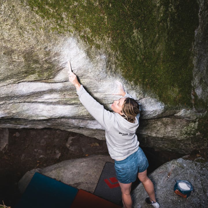 A climber in a Black Diamond Hoody brushes a chalky boulder. 