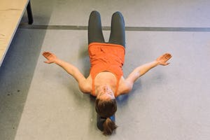woman lying on ground, arms in low position