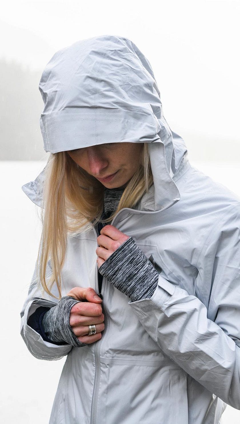 A woman zipping up the Stormline Stretch Rain Shell that she is wearing