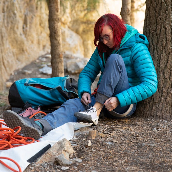 A climber wears a Black Dimond puffy to stay warm while lacing up their Black Diamond Momentum climbing shoes. 