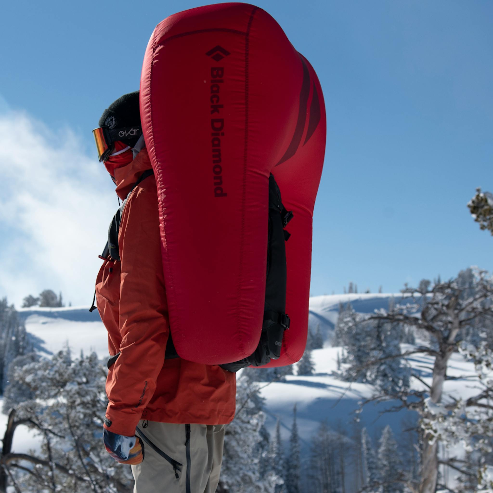 A snowboarder stands away from the camera in a deloyed Jetforce split pack.