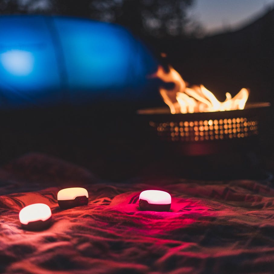 Three shining Moji lanters on a blanket in front of a tent and a campfire at night