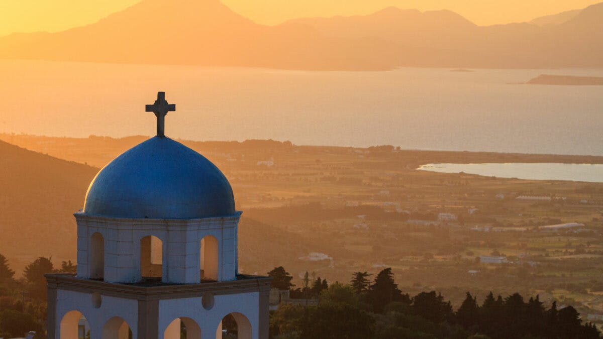 una chiesa bianca e blu si staglia sul panorama di kos al tramonto, ecco cosa vedere sull'isola