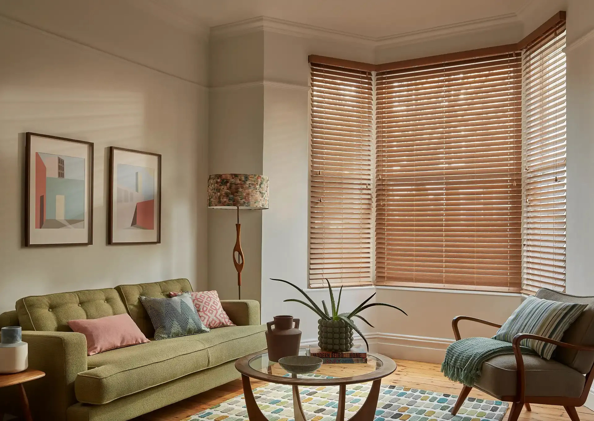 Wooden venetian blinds filtering sunlight and casting striped shadows across a cozy living room with sofa, cushions, floor lamp, coffee table and plant; visible