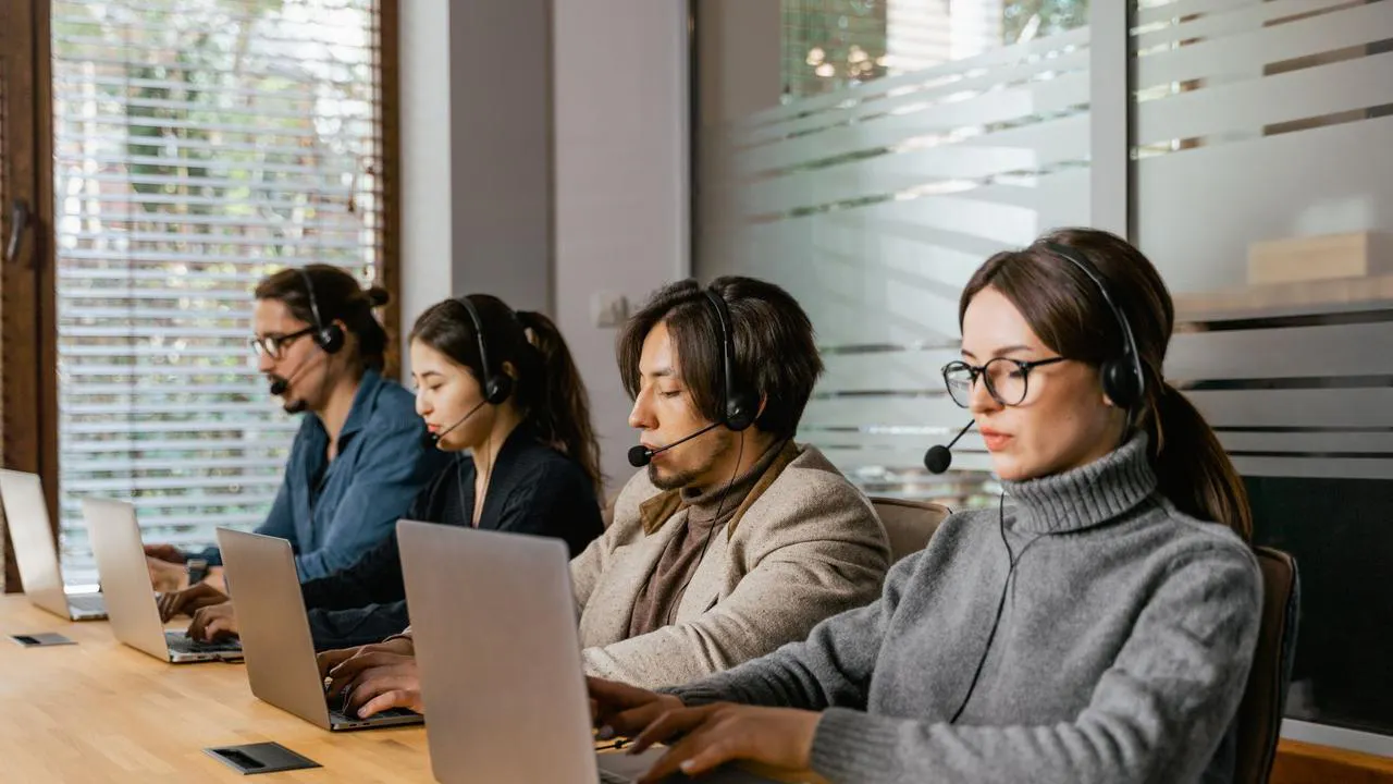 Equipe de suporte ao cliente diversa em um escritório moderno, cada membro usando computador e smartphone para comunicação multi-canal.