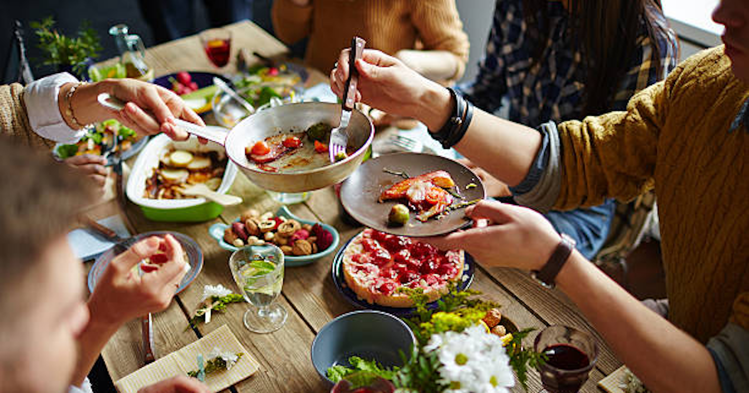 Table pleine de nourriture et personnes se servant et partageant les différentes assiettes