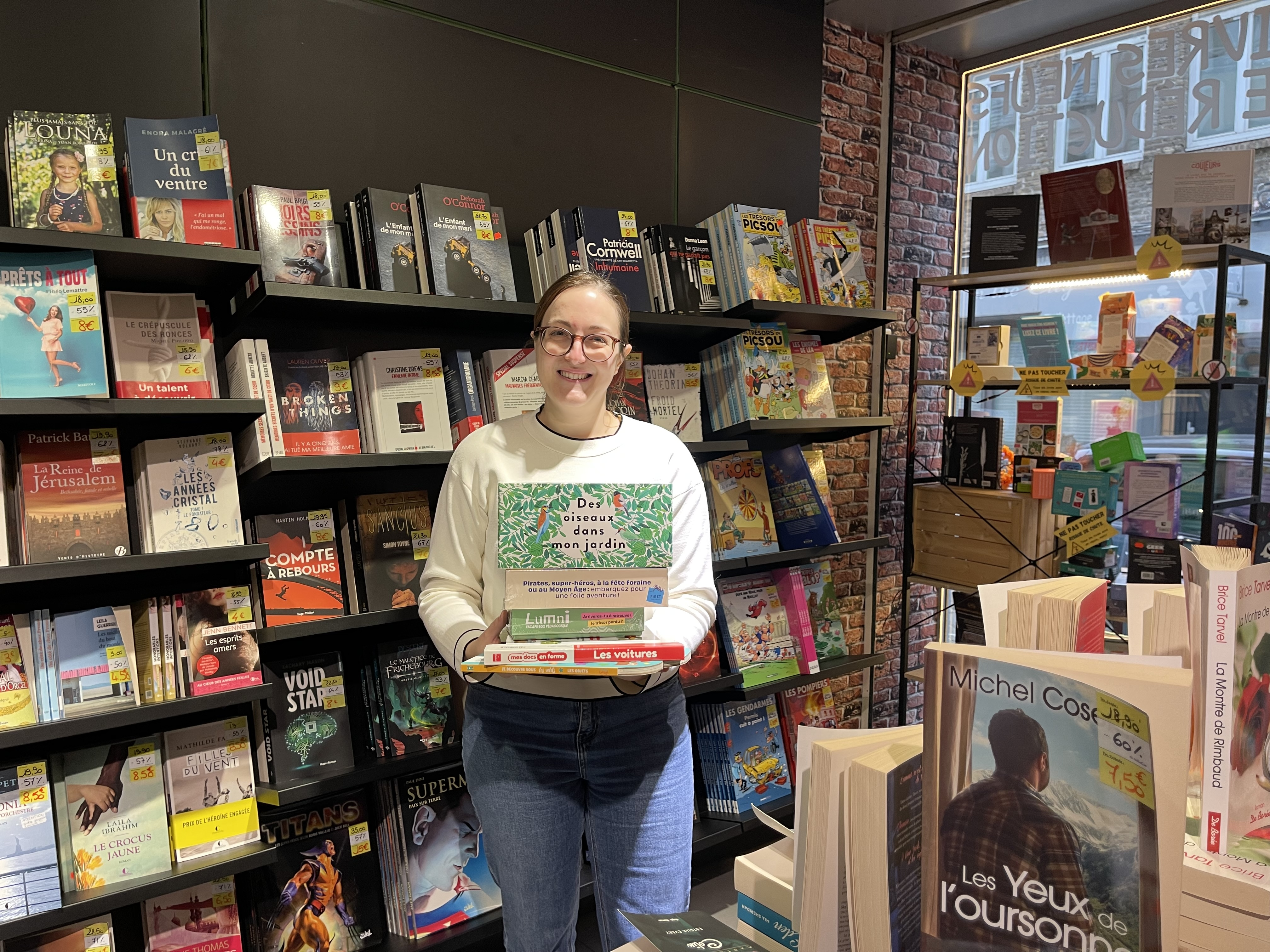 Femme dans une librairie qui tient une pile de livres dans les mains