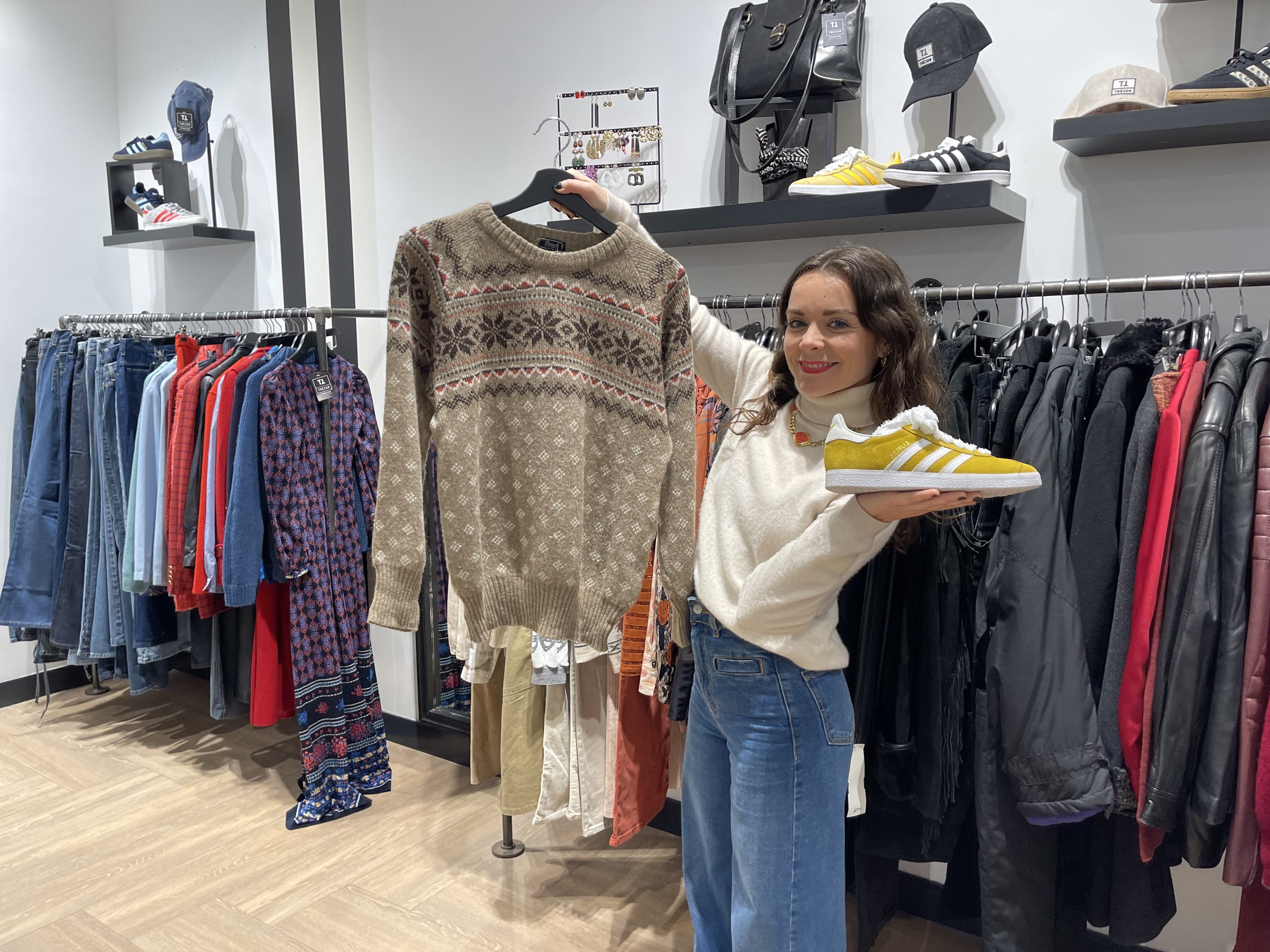 Une jeune femme qui tient un pull dans une main et une chaussure dans l'autre dans une boutique de vêtement