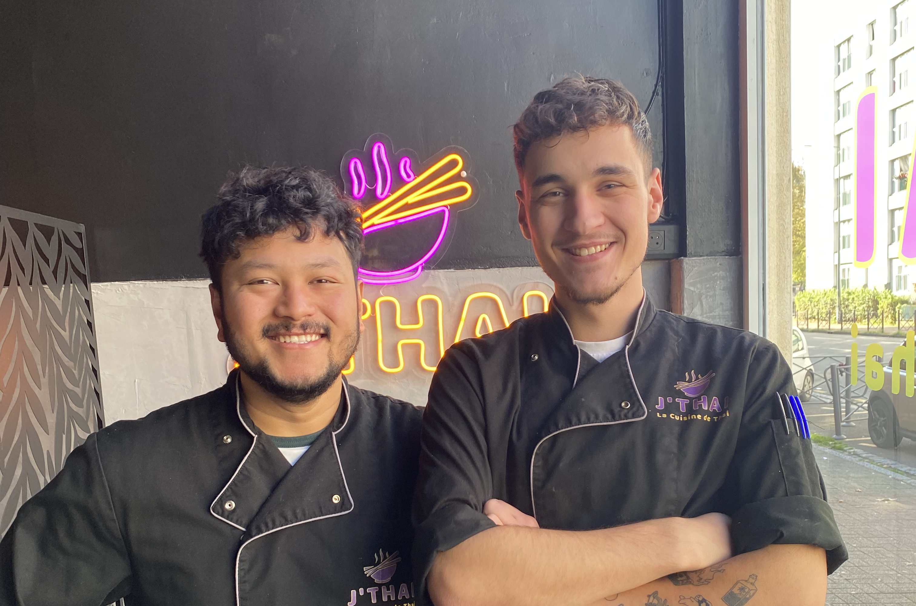 2 hommes avec un tablier noir qui posent dans une cuisine